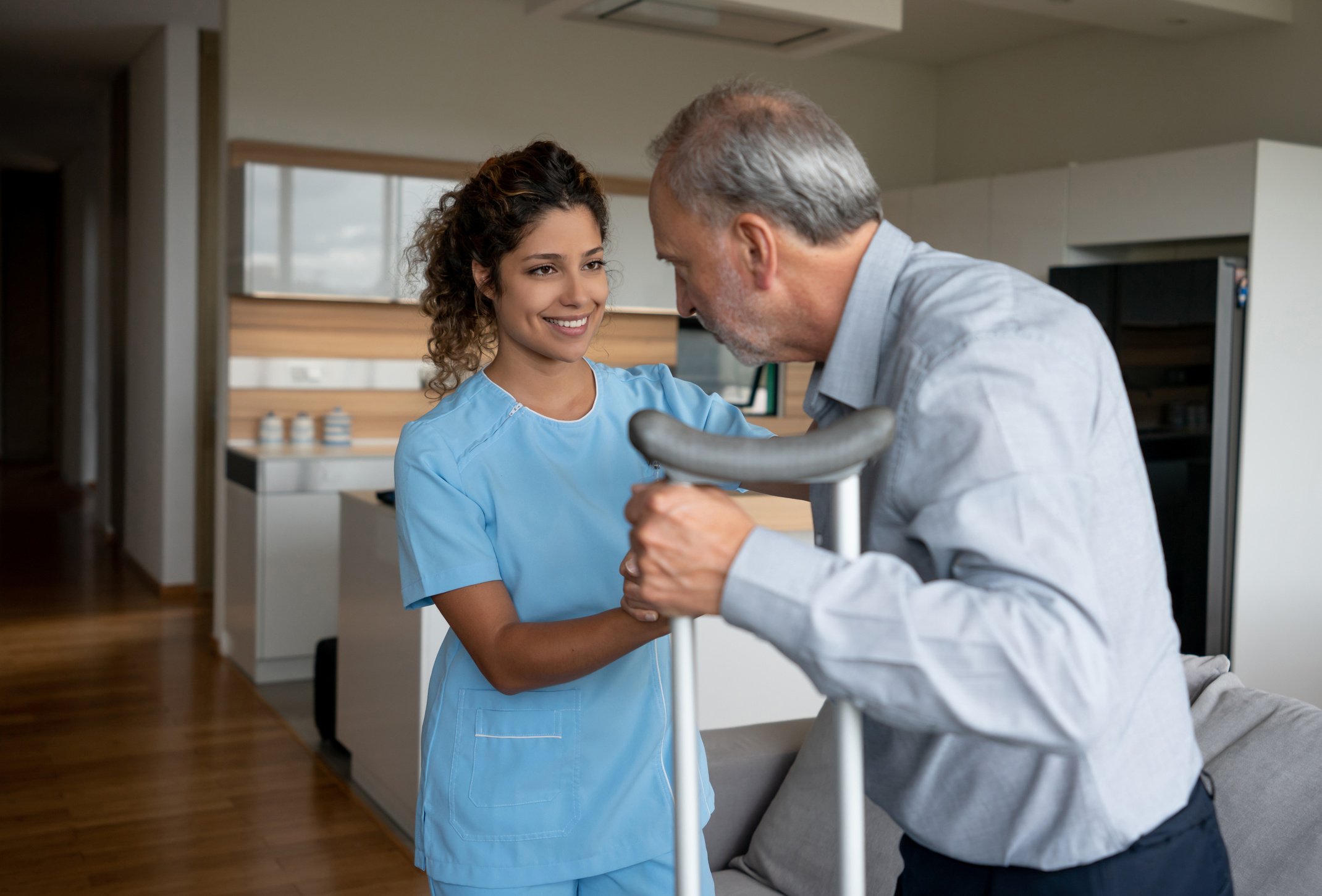 Home caregiver helping a senior man in crutches at home